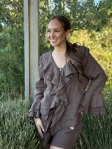 Camisa de lino azul marino con volados en cascada a lo largo del frente y en los puños de las mangas largas. Presenta un escote en V con un botón de nácar visible.