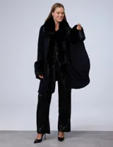 Ruana de tejido color tostado con cuello, bordes frontales y puños amplios con apliques de piel sintética al tono. Presenta una abertura central con cierre de botón tipo trenca.