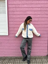 Chaqueta color crema de corderito con detalles en jean azul en cuello, solapa, bolsillos y puños.