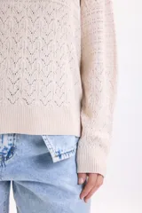 Sweater de punto fantasía color crudo, de corte holgado, con cuello redondo y mangas largas.