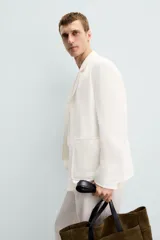 Blazer color blanco confeccionado en tejido con mezcla de algodón y lino, de corte recto y holgado. Tiene cuello con solapas de muesca, manga larga con puños abotonados, bolsillos frontales de parche y cierre frontal con botones.