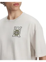 Remera de corte oversize color beige, con cuello redondo acanalado y hombros caídos. Presenta un gráfico estampado en el pecho con el logo de Under Armour integrado en un diseño inspirado en el baloncesto.