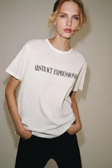 Camiseta oversize blanca de manga corta y cuello redondo, confeccionada en hilatura de algodón con detalle de texto estampado en contraste en el pecho.