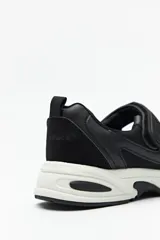 Zapatillas deportivas negras con suela blanca de 4cm de alto y tira ajustable con velcro.