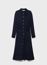 Vestido midi de color negro con cuello camisero y cierre frontal de botones dorados. Presenta mangas largas con puños abotonados, diseño entallado en la cintura con detalle drapeado y falda evasé.