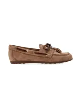 Mocasín náutico de cuero gamuza color camel, con detalles de costuras pespunteadas, cordones de cuero oscuro entrelazados con ojales metálicos dorados y borlas decorativas en el empeine.