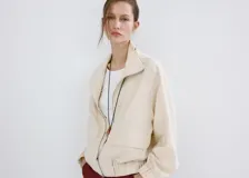 Chaqueta oversize color beige con cuello alto, cierre frontal de cremallera, bolsillos frontales con solapa y mangas largas.