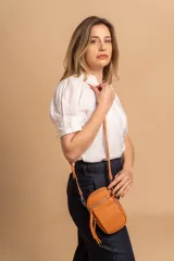 Bandolera compacta color rosado, con correa regulable y desmontable. Tiene apertura superior, bolsillo frontal con cierre y detalle de borla, y bolsillo trasero sin cierre. El interior está forrado en tela y cuenta con un bolsillo adicional.