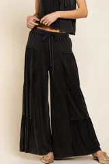 Pantalón negro de tela acanalada con diseño de paneles horizontales que crean un efecto de volados. Presenta corte amplio, cintura elástica con cordón de ajuste y caída fluida.