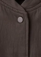 Chaqueta bomber oversize color verde oscuro con cuello mao, manga larga y cierre frontal de botones a presión.