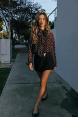 Blusa de cuello subido con lazo en la espalda, manga larga con puños elásticos, forro interior y estampado de lunares negros sobre fondo blanco.