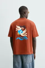 Camiseta de manga corta y cuello redondo, color terracota, con un pequeño bordado de una flor amarilla y la inscripción "Abstract Harmony" en el pecho.