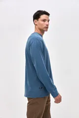 Remera de manga larga color beige, confeccionada en algodón lavado con textura suave. Presenta cuello redondo con detalle de costura en V, corte clásico y estampado pequeño en el pecho con la palabra Uniform.