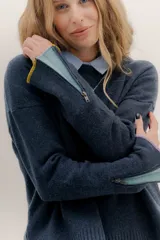 Buzo de lambswool color beige, con escote redondo y detalle en V. Presenta cierres metálicos en los puños que revelan un interior en contraste de color marrón y ribete rojo. Tiene tajos laterales para mayor comodidad y un fit amplio.