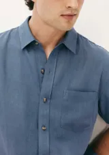Camisa de manga corta con cuello clásico, cierre frontal de botones y bolsillo en el pecho. Presenta un corte entallado y un acabado de textura sutil.