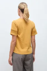 Remera blanca de algodón con cuello en V y mangas cortas que presentan un detalle de puntilla en los bordes.
