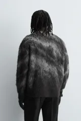 Jersey de corte relajado con cuello redondo y manga larga, confeccionado en tejido cepillado con patrón jacquard en tonos oscuros y acabados en rib.