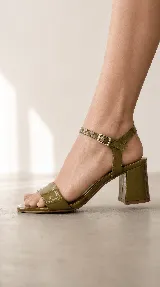 Sandalia de taco cuadrado color dorado, con tira delantera ancha, talón cerrado y tira fina con hebilla ajustable al tobillo.