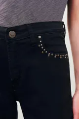 Pantalón de jean negro, corte slim, con tachas metálicas plateadas decorando la abertura de los bolsillos delanteros.