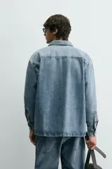 Sobrecamisa de denim de algodón con efecto lavado, corte regular fit, cuello solapa, cierre frontal de botones, manga larga con puños abotonados y dos bolsillos frontales con solapa en el pecho.