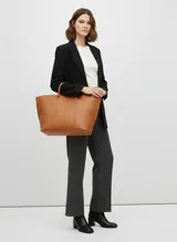 Bolso shopper de efecto cuero color coñac, de gran tamaño, con asas cortas para llevar en mano y correa ajustable para llevar al hombro. Presenta un diseño liso con costuras verticales marcadas en el frente.