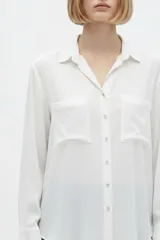 Camisa de seda negra de corte holgado, con cuello camisero y escote en V, cierre frontal con botones y dos bolsillos en el pecho.