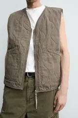Chaleco acolchado de algodón color verde militar, de corte relaxed fit, con cuello en V, cierre frontal con cremallera y bolsillos de parche en la cadera. Presenta diseño acolchado con pespuntes ondulados y efecto lavado.