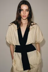 Kimono Zara Woman Collection de manga corta y cuello en V, confeccionado en tejido color crudo con sutiles rayas verticales. Presenta aplicaciones de terciopelo negro a contraste en la solapa y un fajín ancho integrado en la cintura.