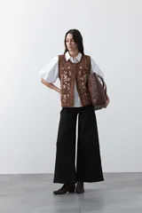 Chaleco tejido color marrón con bordados artesanales de motivos florales y geométricos en color crema. Presenta cuello redondo, cierre frontal con botones y diseño sin mangas.