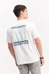 Remera blanca de manga corta y cuello redondo, confeccionada en 100% algodón. Presenta una estampa grande en la espalda con diseño floral en tonos verdes y texto azul con la frase 'Botanical Worldwide Creative Club'.