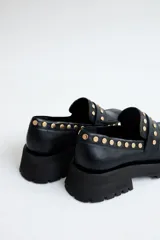 Mocasines de cuero color marrón con suela track negra y tachas doradas.