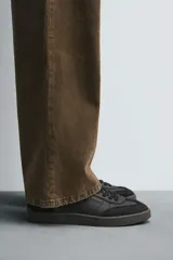 Zapatilla deportiva de estilo retro, color negro, con parte superior fabricada en combinación de piezas de cuero liso y gamuza perforada. Presenta una suela de goma en color marrón oscuro o ahumado en contraste.