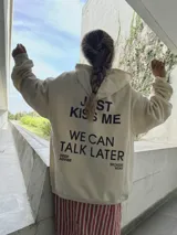 Canguro beige de algodón con capucha, cordones ajustables y estampa en pecho y espalda con la frase "Just Kiss Me We Can Talk Later".