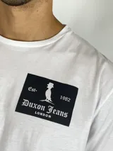 Remera blanca de manga corta con cuello redondo y estampa rectangular negra en el pecho con el logo y nombre de la marca Duxon Jeans.