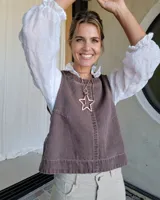 Chaleco de corte recto y holgado en color marrón, confeccionado en tejido de algodón con textura similar al denim. Presenta costuras verticales decorativas en el frente y un diseño minimalista sin mangas.