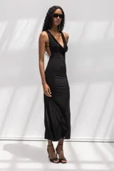 Vestido largo negro de corte al cuerpo, con escote halter y cuello drapeado. Presenta una silueta entallada que se ensancha suavemente hacia el ruedo.