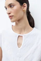Remera de manga corta color verde petróleo, con cuello redondo y detalle de abertura tipo gota en el frente. Presenta un diseño con bordados geométricos tono sobre tono en la parte frontal.