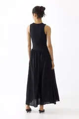 Vestido midi negro sin mangas, con cuello redondo y diseño ajustado en la parte superior de punto acanalado. Cuenta con una costura fruncida en diagonal bajo la cintura y una falda larga con vuelo de tejido fluido.