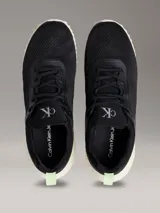 Zapatillas tipo runner Calvin Klein en color negro con suela de EVA blanca y detalles en verde claro en el talón. Presentan diseño tipo calcetín, parte superior de malla técnica y logo de la marca en la lengüeta y el lateral.