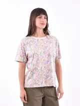 Remera de manga corta con estampado floral en tonos pastel de lila, naranja y verde sobre fondo blanco.
