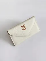 Billetera de cuero vacuno color crudo con textura granulada. Presenta un diseño tipo sobre con cierre de broche y un detalle decorativo de espiga bordado en cuero color suela en la solapa frontal.