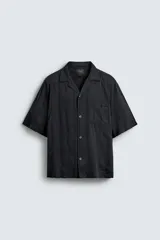 Camisa de algodón negro, de corte relajado (relax fit), con cuello bowling, manga corta y bolsillo plastrón en el pecho. Cierre frontal con botones a presión.