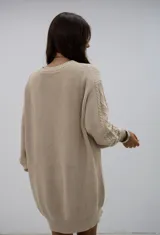 Vestido corto de punto en color beige, con diseño de trenzas en las mangas y cuello redondo. Presenta un corte holgado y puños acanalados.