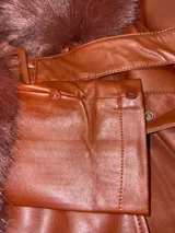 Tapado de cuero sintético color bordó, con cuello y puños de piel sintética desmontables. Presenta cierre frontal con botones y cinturón ajustable con hebilla forrada en el mismo material.