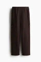 Pantalón marrón de corte holgado con piernas amplias y bolsillos al bies. Modelo de tiro bajo con elástico revestido y cordones para ajustar enlazados a los lados, decorados con cuentas en los extremos.