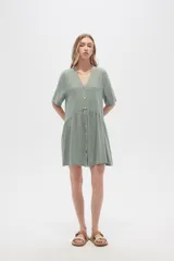Vestido corto de algodón color verde, con cuello en V, cierre frontal de botones y diseño holgado con falda fruncida.