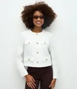 Chaqueta de manga larga confeccionada en tejido tweed, con cuello redondo y cierre frontal mediante botones metalizados. Presenta bolsillos frontales con solapa y botones decorativos a juego.