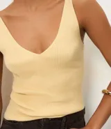 Blusa sin mangas de punto acanalado color crema, con escote en V y espalda descubierta. Confeccionada en una mezcla de viscosa y poliamida, presenta un ajuste al cuerpo y textura vertical en relieve.