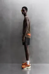 Pantalón corto deportivo color marrón oliva, confeccionado en tejido técnico ligero y elástico, con forro interior. Presenta cintura elástica ajustable con cordón, bolsillos frontales, bolsillo de seguridad trasero con cierre y aberturas laterales en el bajo.