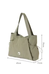 Cartera tipo tote bag de nylon color negro, con bolsillos laterales con cordón ajustable, asas de hombro y detalle de etiqueta frontal.